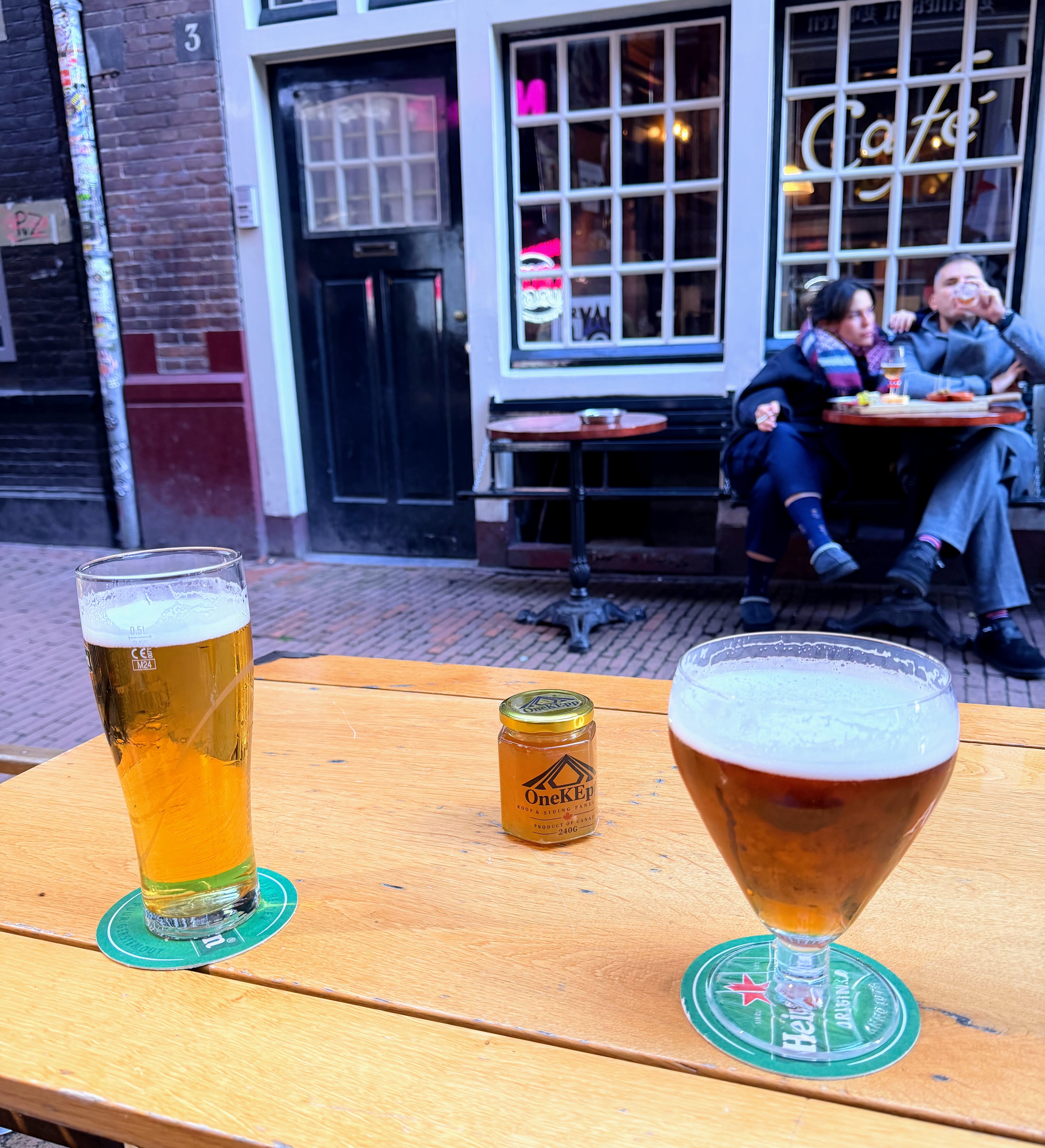 OneKEpp honey jar between two beers on a wooden table at an Amsterdam street café