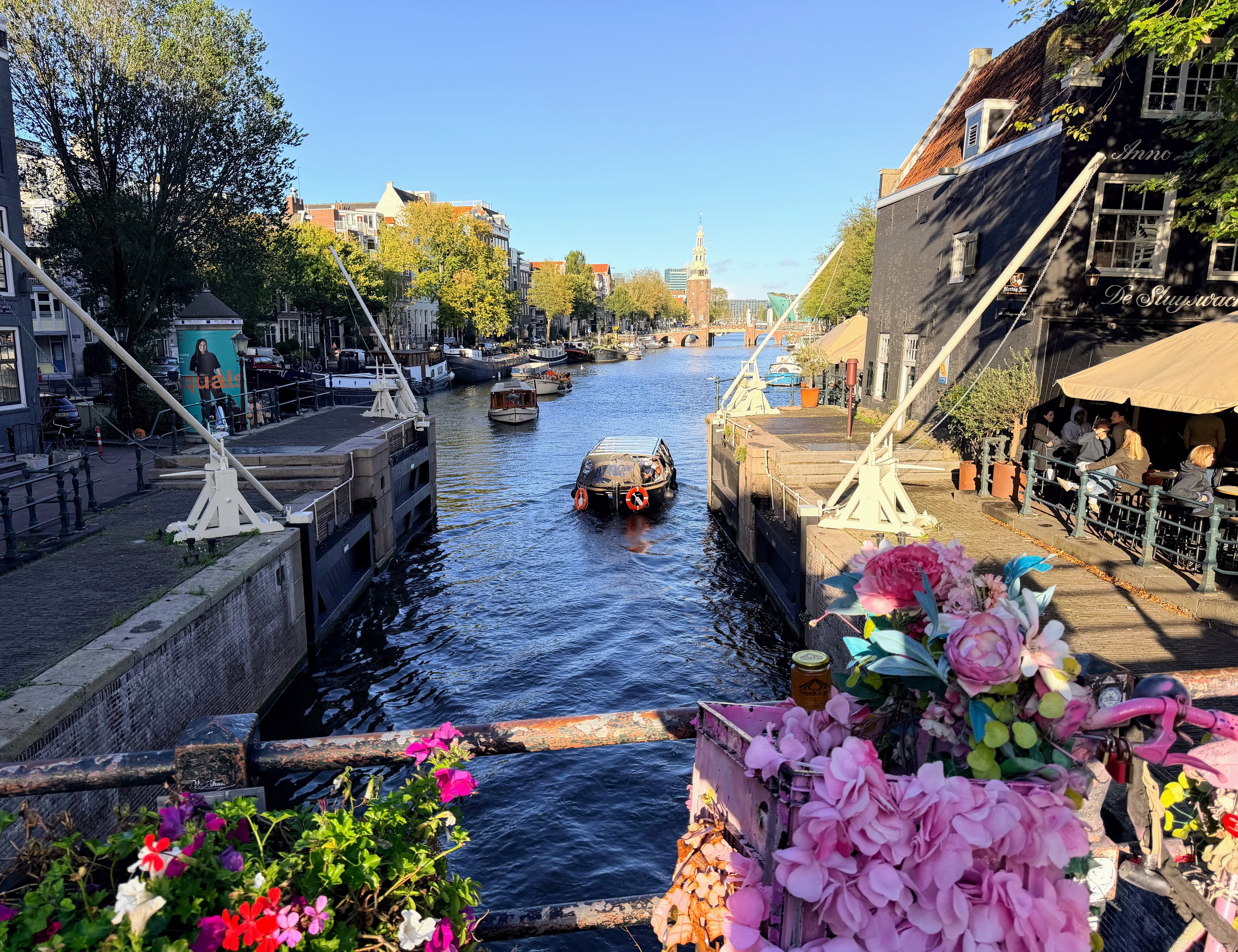 OneKEpp honey jar on a flower-adorned bicycle railing at an Amsterdam canal lock with the Montelbaanstoren tower