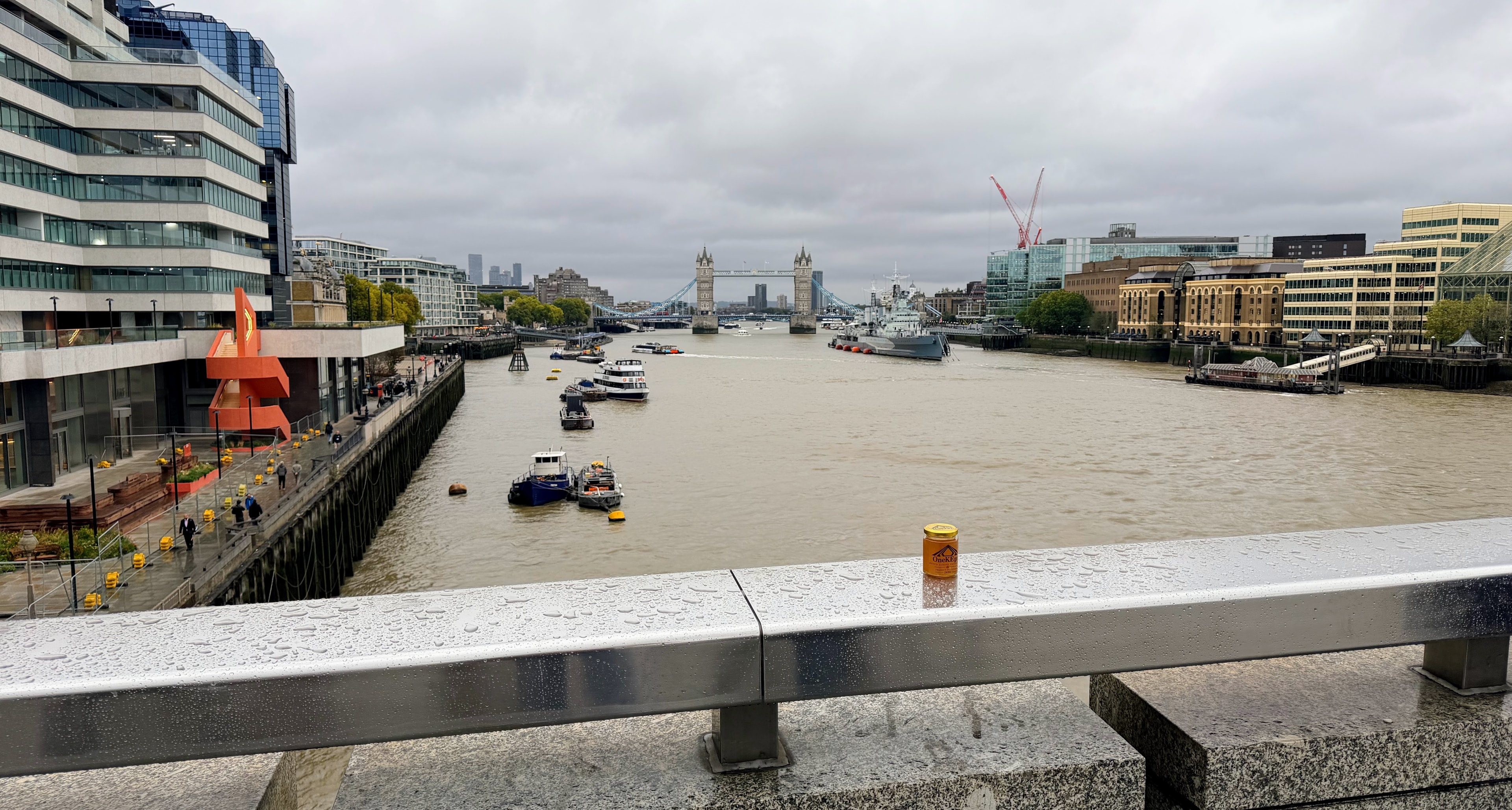 OneKEpp honey jar on a wet railing with Tower Bridge and the Thames in the background